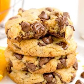 close up shot of orange chocolate chip cookies stacked on top of each other on a plate