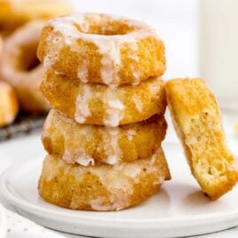 close up shot of Sour Cream Donuts topped with glaze and stacked on top of each other on a plate