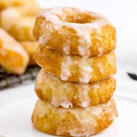 close up shot of Sour Cream Donuts topped with glaze and stacked on top of each other on a plate