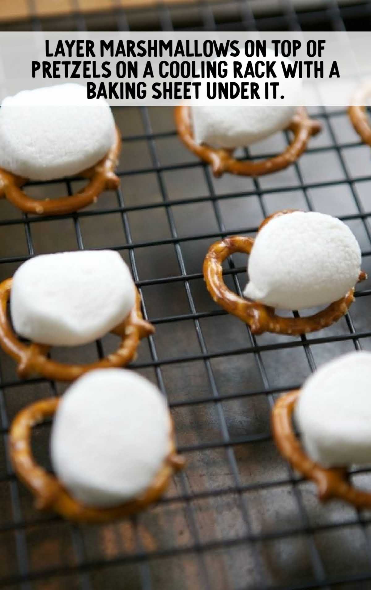 Marshmallows placed on top of mini pretzels on a wire cooling rack with a baking sheet underneath.