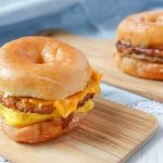 A doughnut sitting on top of a wooden cutting board, with Breakfast sandwich