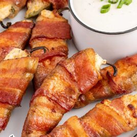 close yup shot of Bacon-Wrapped Jalapeño Poppers on a plate with a side of dressing