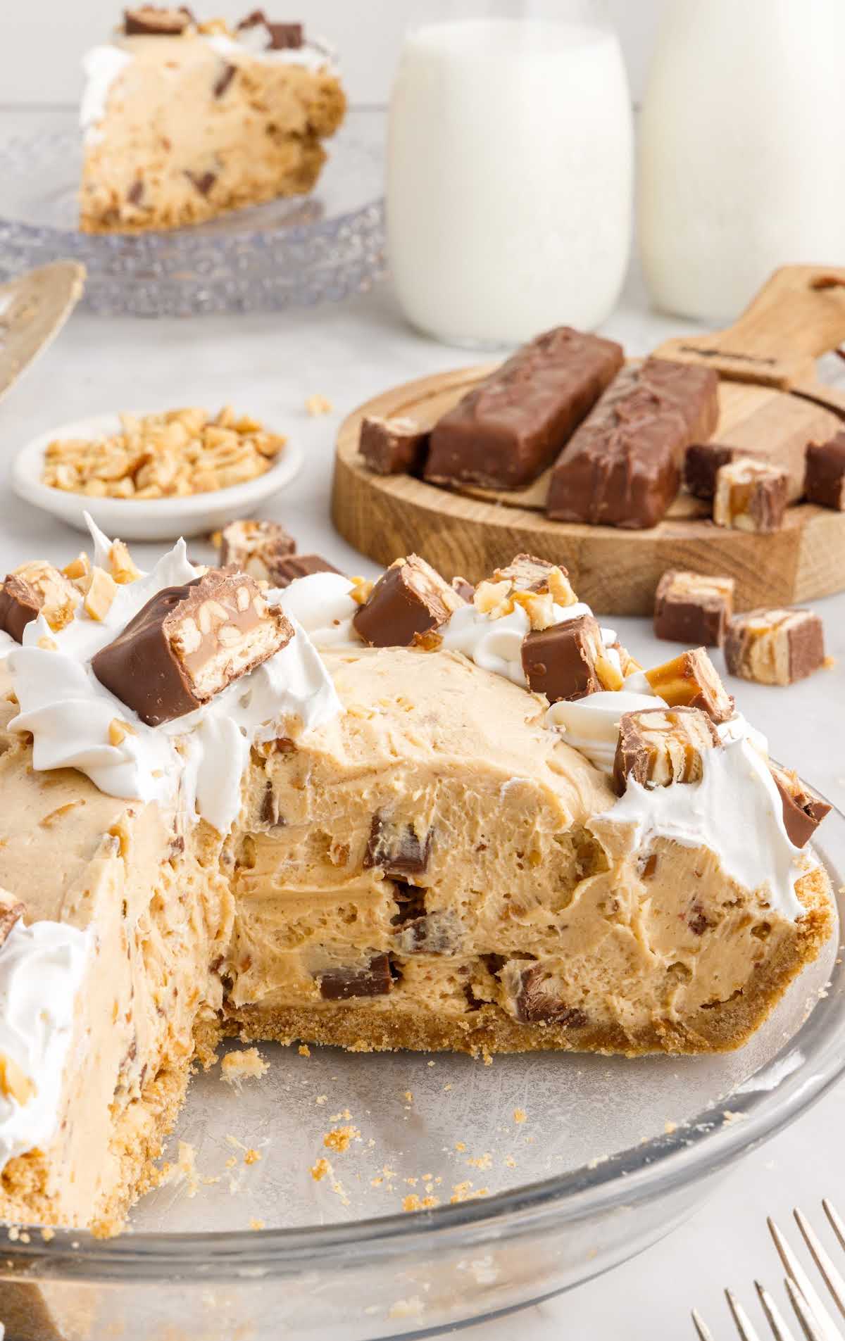 close up shot of a baking dish of pie topped with pieces of snickers with a slice missing