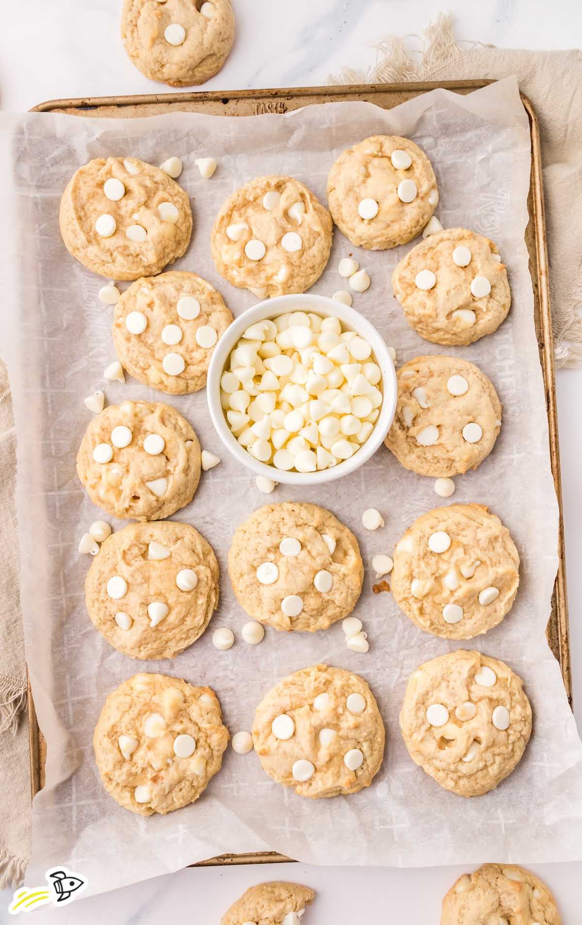overhead shot of White Chocolate Chip Cookies on a baking sheet with a bowl of white chocolate chips