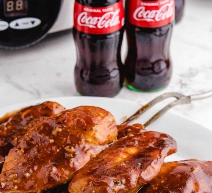 close up shot of slow cooker Coca Cola chicken topped with bbq sauce on a white plate