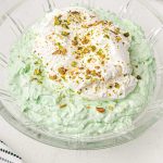 close up shot of a large bowl of pistachio salad topped with whipped cream and crushed pistachios