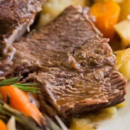 close up shot of instant pot pot roast served over carrots and potatoes on a plate