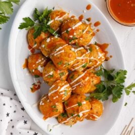 close up overhead shot of a plate of Buffalo Chicken Meatballs drizzled with buffalo sauce and ranch dressing and sprinkled with parsley and blue cheese crumbles