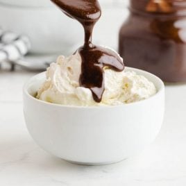 close up side shot of hot fudge sauce being poured with a spoon on to vanilla ice cream in a bowl