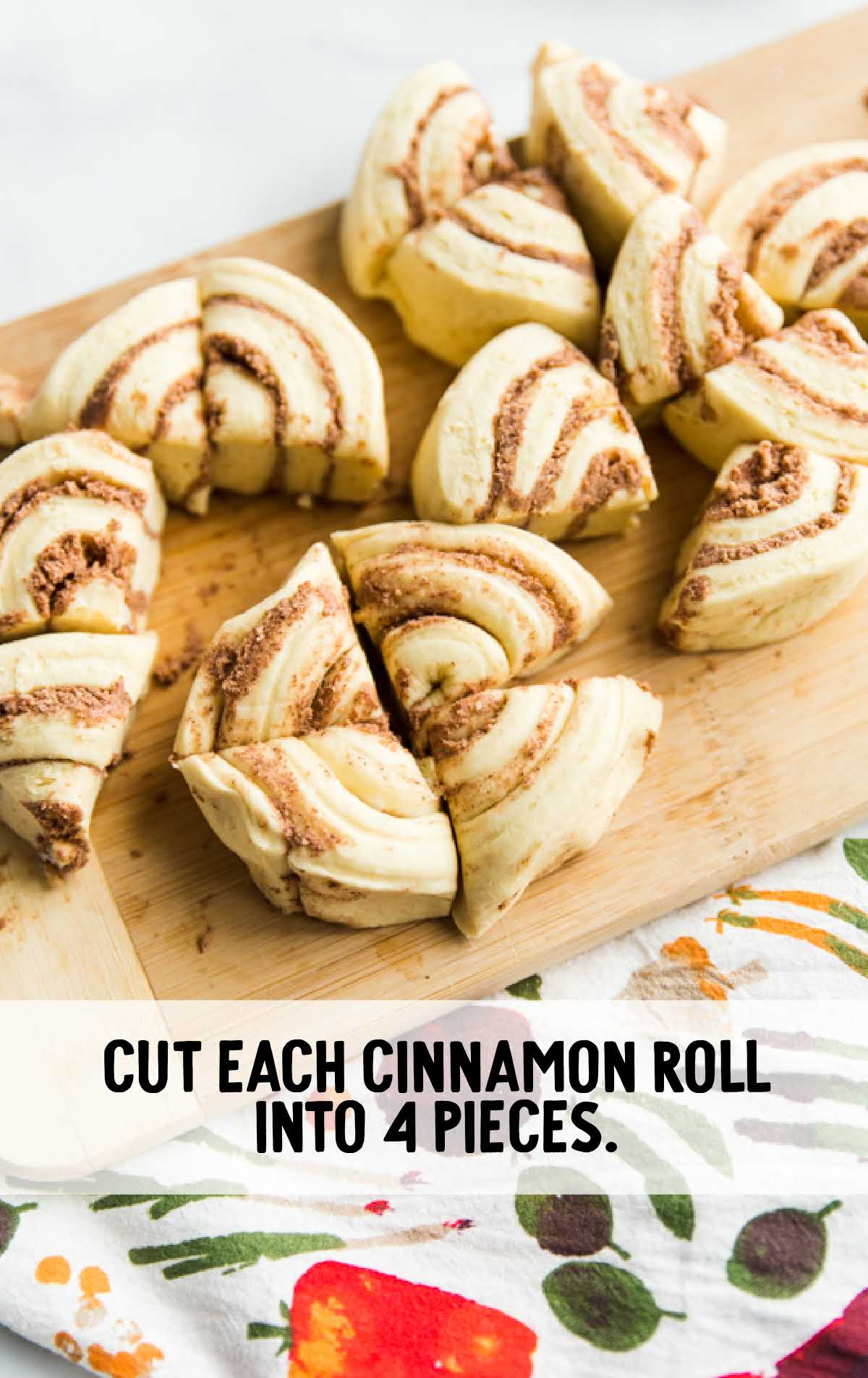 Cinnamon rolls cut into quarters on a wooden cutting board with instruction to cut each into 4 pieces