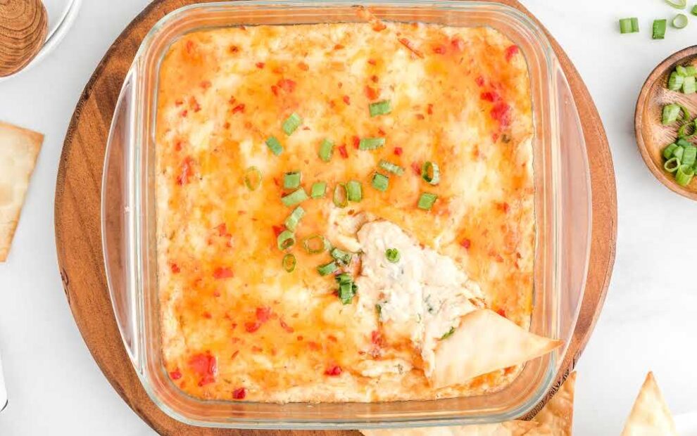 close up overhead shot of a baking dish of Crab Rangoon Dip garnished with green onions with a chip being dipped into it