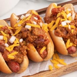 Homemade chili dogs made with hot dog chili, hot dogs, buns, shredded cheese, and onions