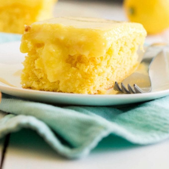 close up side shot of lemon poke cake on a white plate with a fork