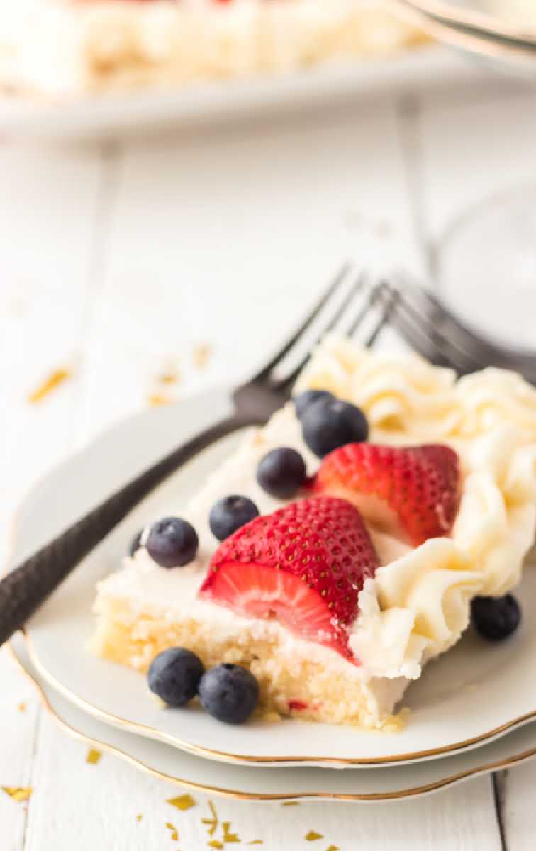 close up shot of a slice of American flag cake topped with strawberries and blueberries on a plate