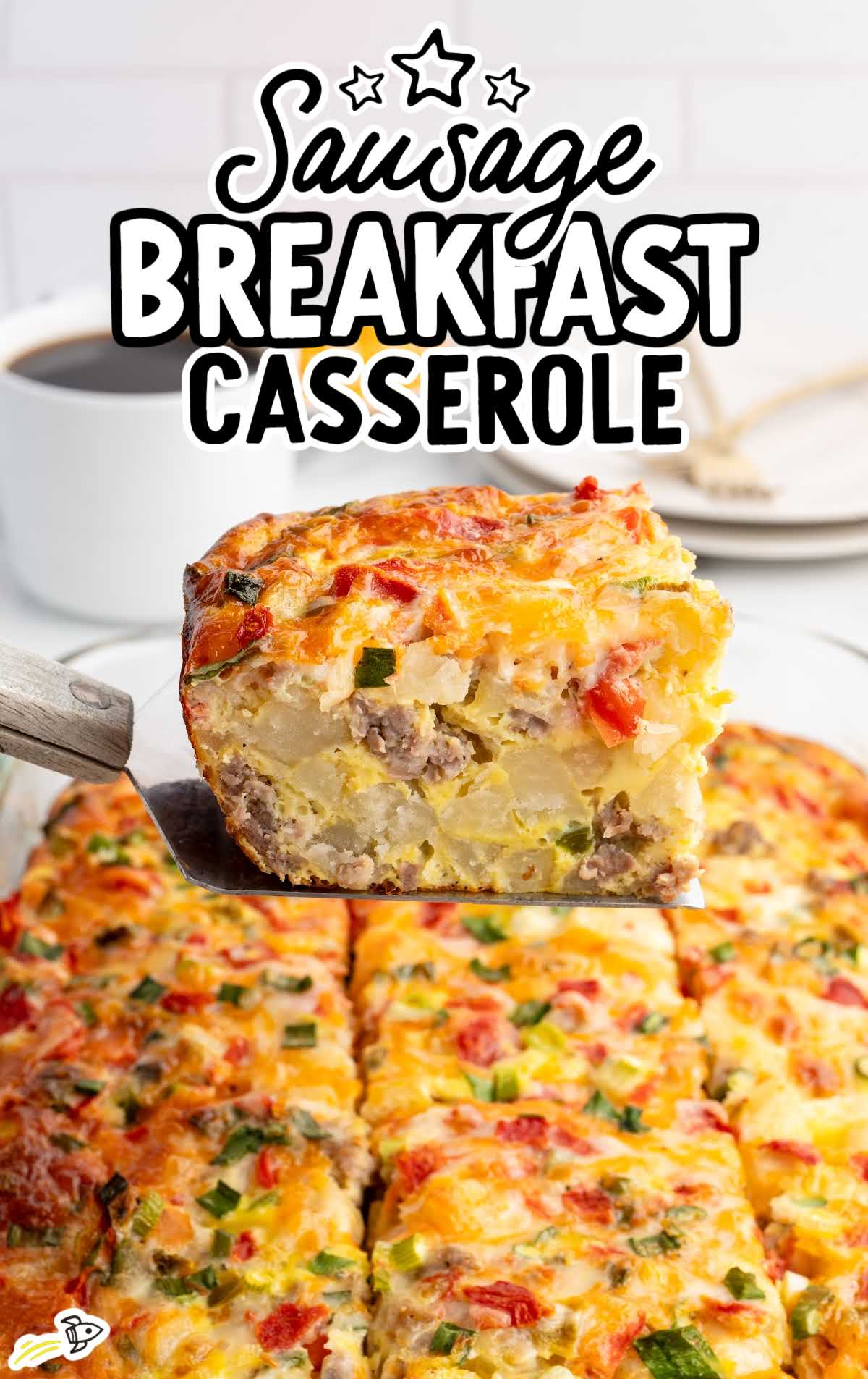 Spatula lifting a hearty slice of sausage breakfast casserole from baking dish with coffee cup in background.