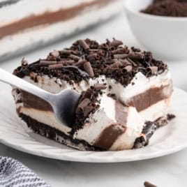 A fork taking a bite from a layered chocolate and cream dessert with chocolate shavings on top, served on a white plate—just like the ultimate Chocolate Lasagna Recipe.