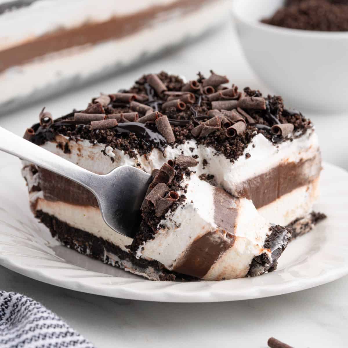 A fork taking a bite from a layered chocolate and cream dessert with chocolate shavings on top, served on a white plate—just like the ultimate Chocolate Lasagna Recipe.