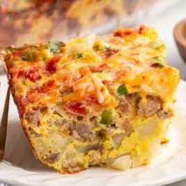 Slice of sausage breakfast casserole on a plate showing layers of eggs, sausage, diced potatoes, and melted cheese.