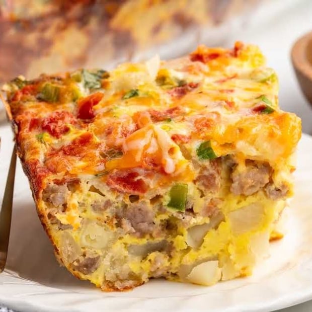 Slice of sausage breakfast casserole on a plate showing layers of eggs, sausage, diced potatoes, and melted cheese.