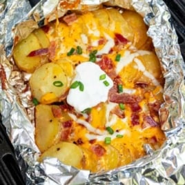 Foil packet of sliced potatoes grilled with melted cheese, bacon, sour cream, and green onions.