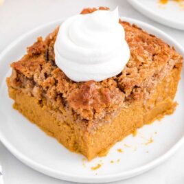 close up shot of a slice of Pumpkin Dump Cake topped with whipped cream on a plate