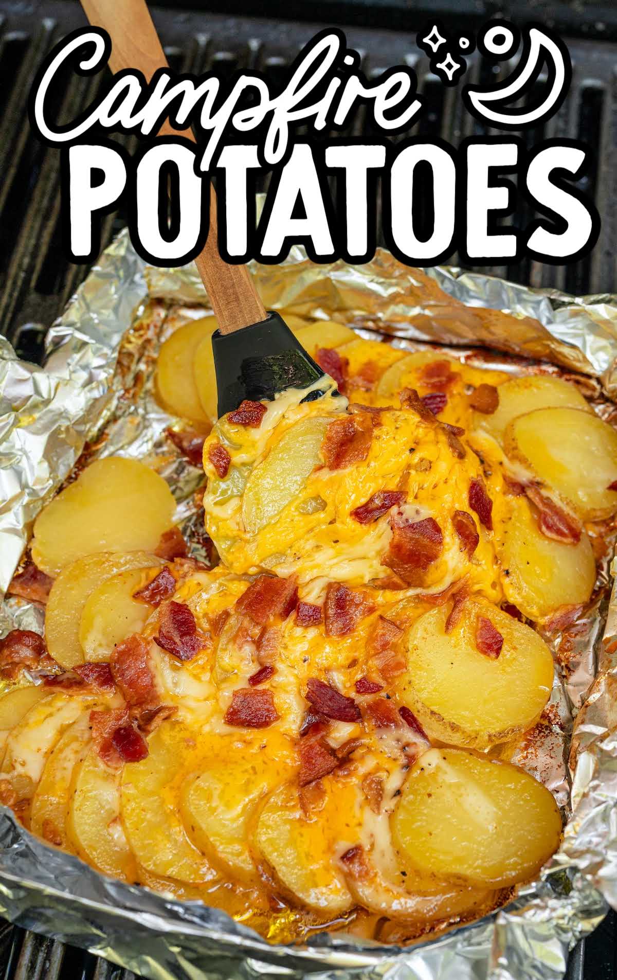 Spatula lifting cheesy campfire potatoes with bacon from a foil packet on the grill.