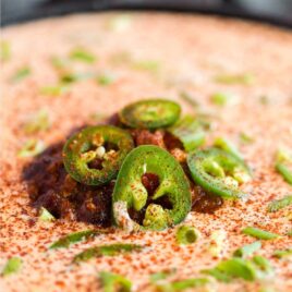 close up shot of a bowl of Chili Cheese Dip topped with green onions and jalapeños
