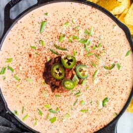 close up overhead shot of a bowl of Chili Cheese Dip topped with green onions and jalapeños