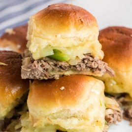 close up shot of Philly cheesesteak sliders stacked on top of each other on a white plate