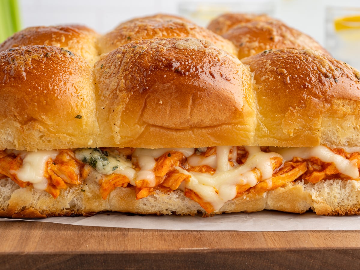 A close-up of a Buffalo Chicken Sliders Recipe featuring soft, golden dinner rolls filled with shredded chicken and melted cheese, resting on a wooden surface.