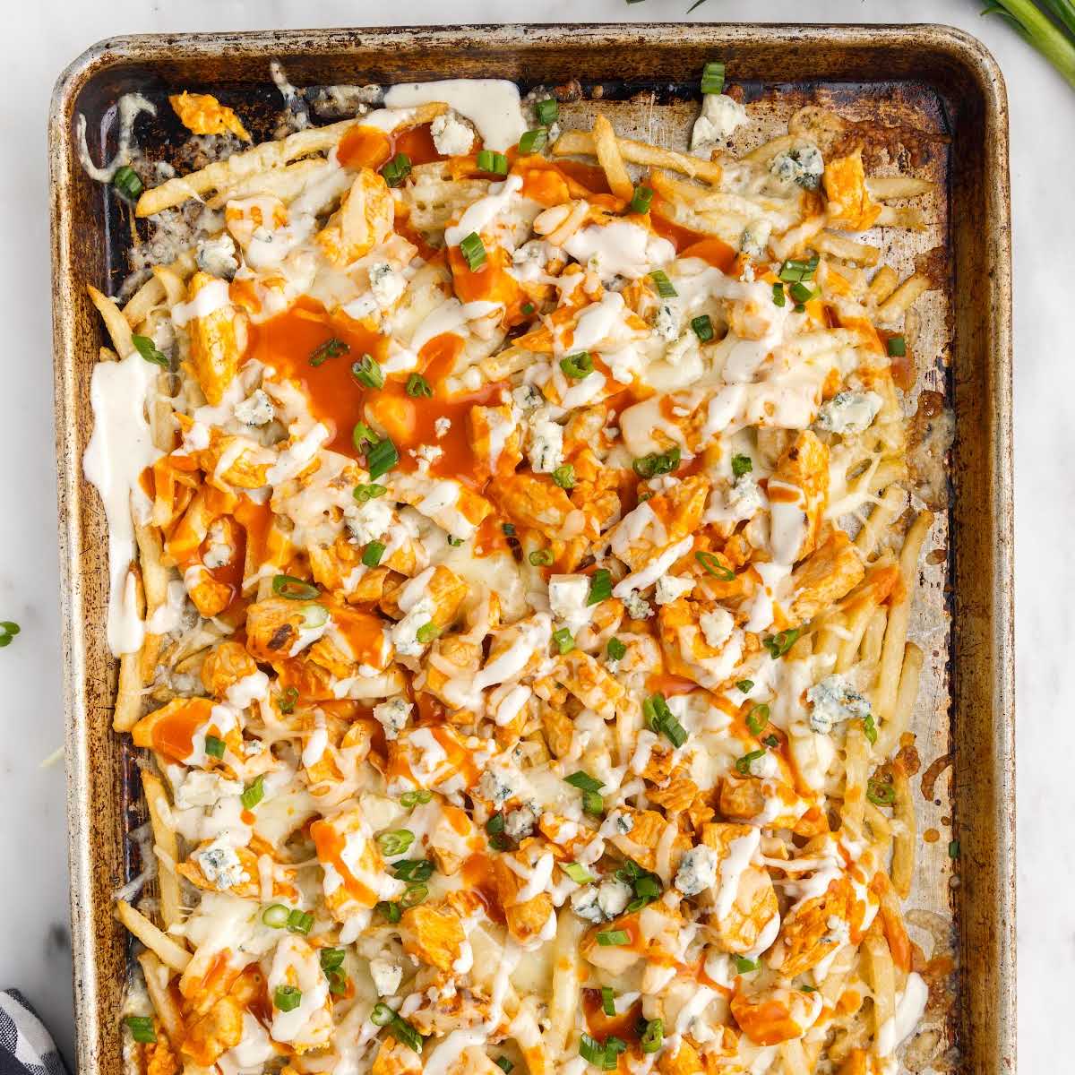 close up overhead shot of a sheet pan of Buffalo Chicken Fries topped with buffalo sauce and ranch then garnished with green onions