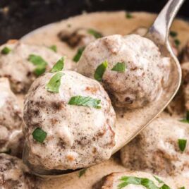 close up shot of a spoonful over a crockpot full of meatballs garnished with parsley