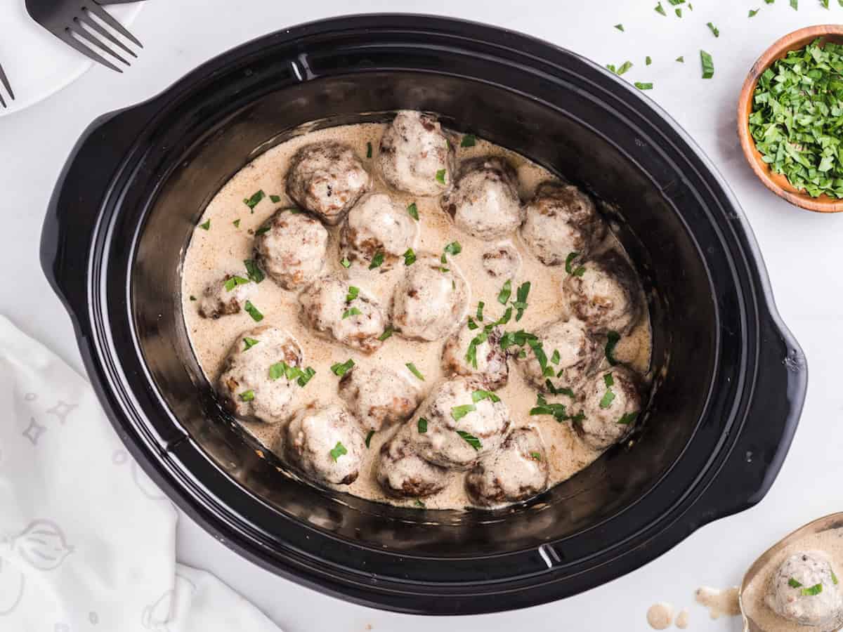Crockpot Swedish meatballs in a creamy sauce, garnished with fresh herbs.