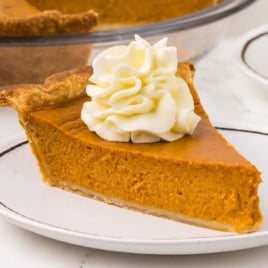 a slice of Pumpkin Pie topped with whipped cream on a plate