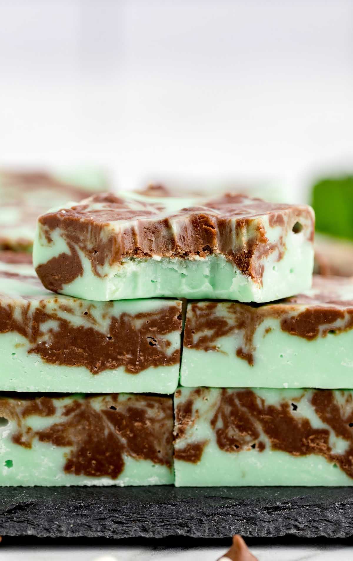 a close up shot of Mint Chocolate Fudge bars stacked on top of each other with one having a bite taken out of it