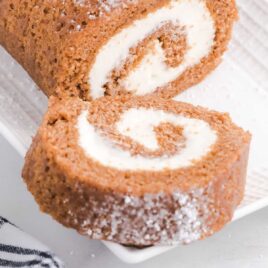 close up shot of pumpkin roll with a slice removed on a serving tray
