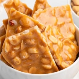 Bowl of golden brown peanut brittle pieces with crunchy roasted peanuts