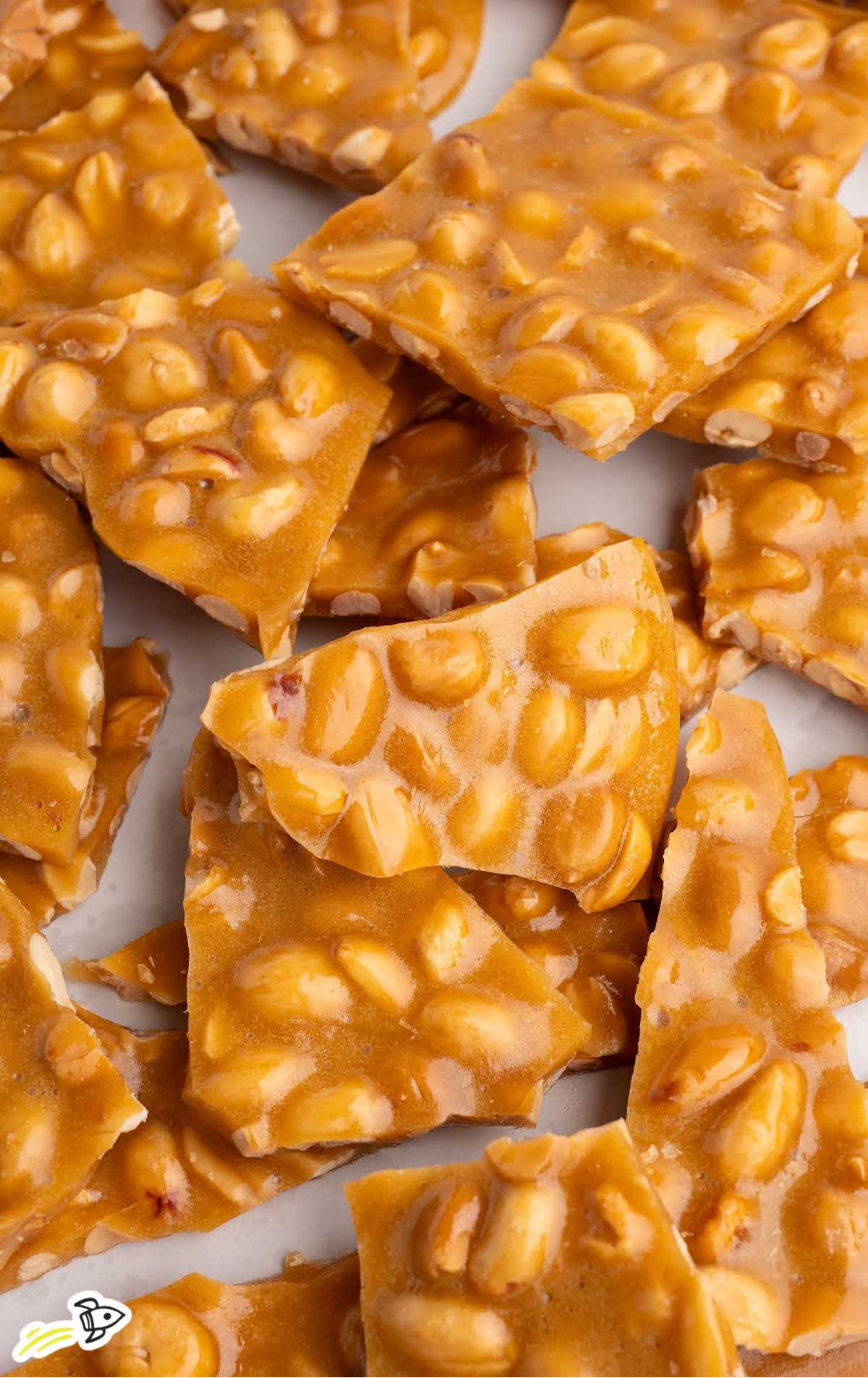 Scattered peanut brittle squares on a white surface showing caramelized coating