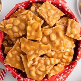 Overhead view of a red holiday-lined basket filled with golden homemade peanut brittle pieces