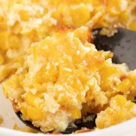 close up shot of a serving of Corn Pudding being picked up from the dish with a large spoon