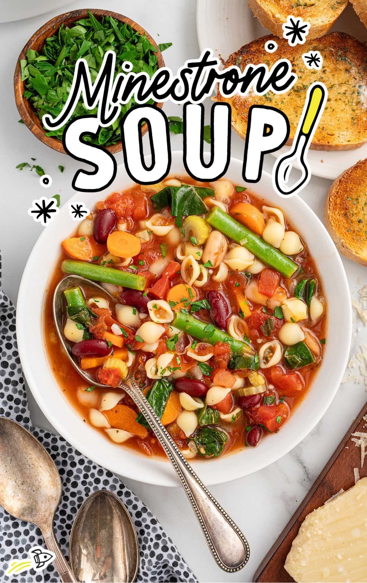 Bright and colorful bowl of minestrone soup with vegetables, pasta, and beans, served with toasted garlic bread on a marble surface.