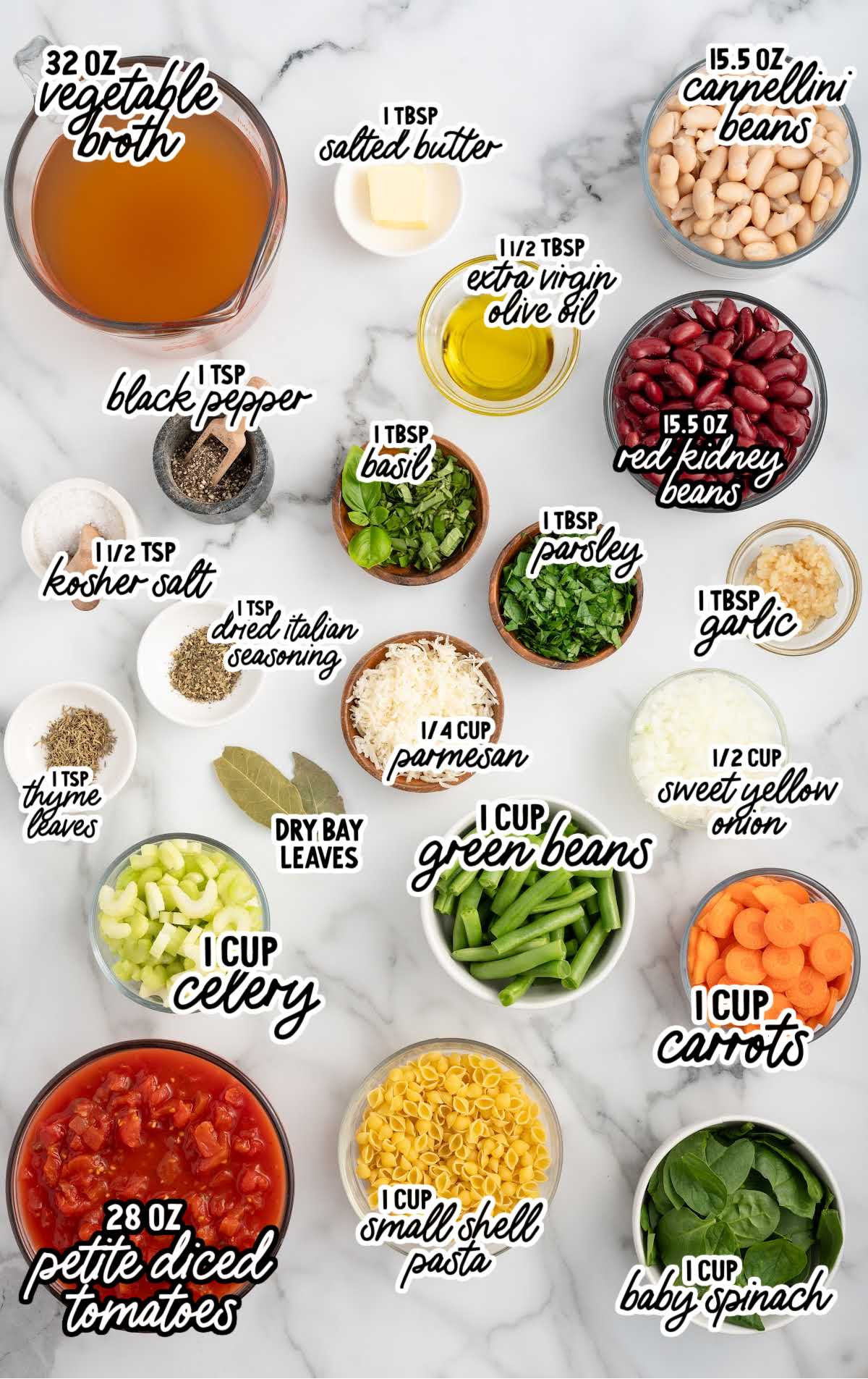 Flat lay of labeled minestrone soup ingredients including vegetables, beans, pasta, herbs, spices, and broth arranged on a white surface.