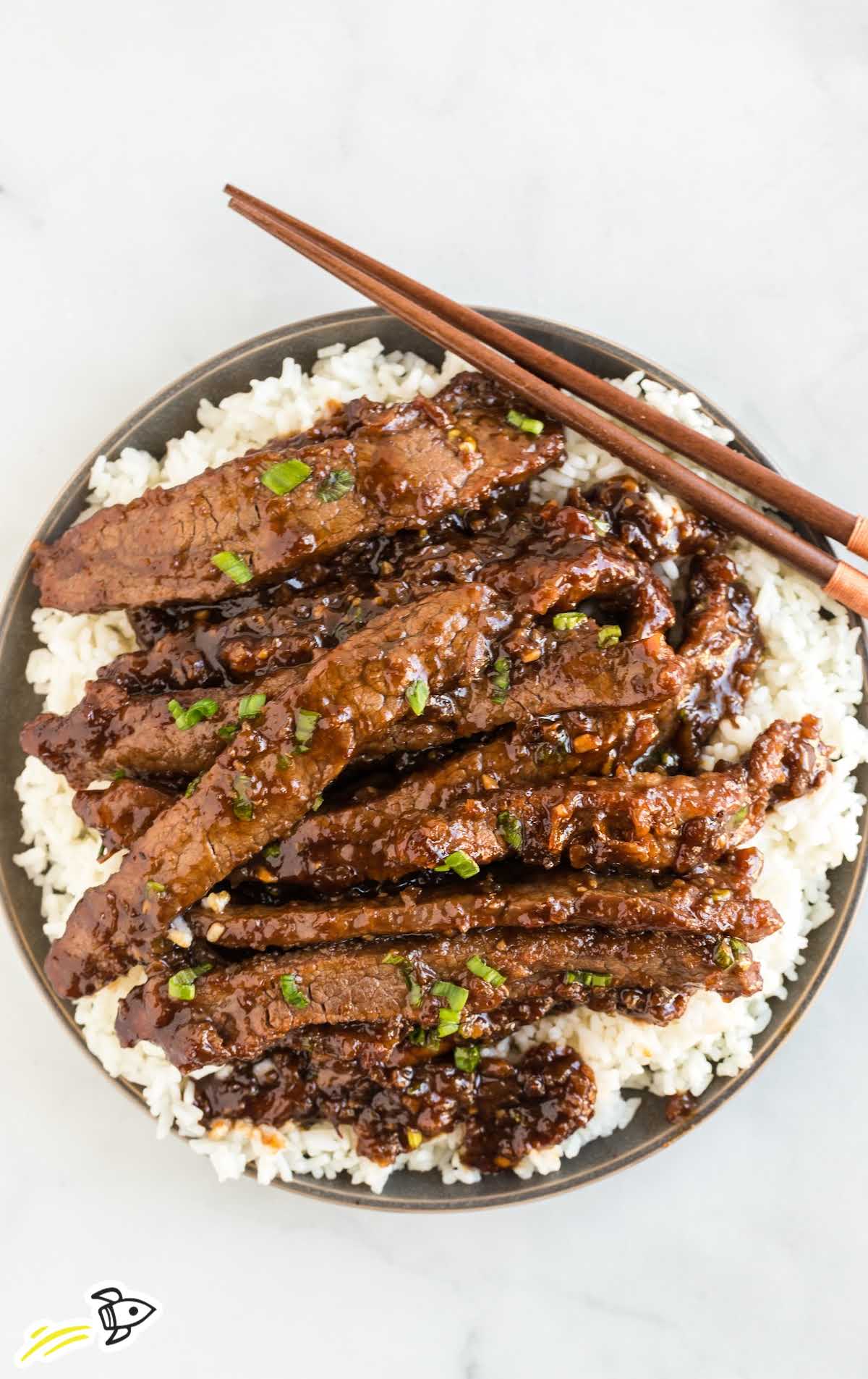 close up shot of a plate of Mongolian Beef garnished with green onions and served over white rice