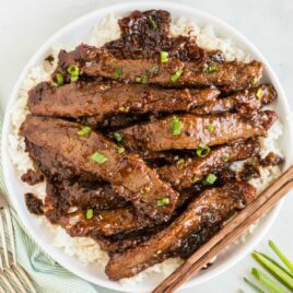 close up overhead shot of a plate of Mongolian Beef garnished with green onions and served over white rice with chopsticks