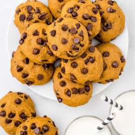 close up overhead shot of a plate of Pumpkin Chocolate Chip Cookies and glasses of milk