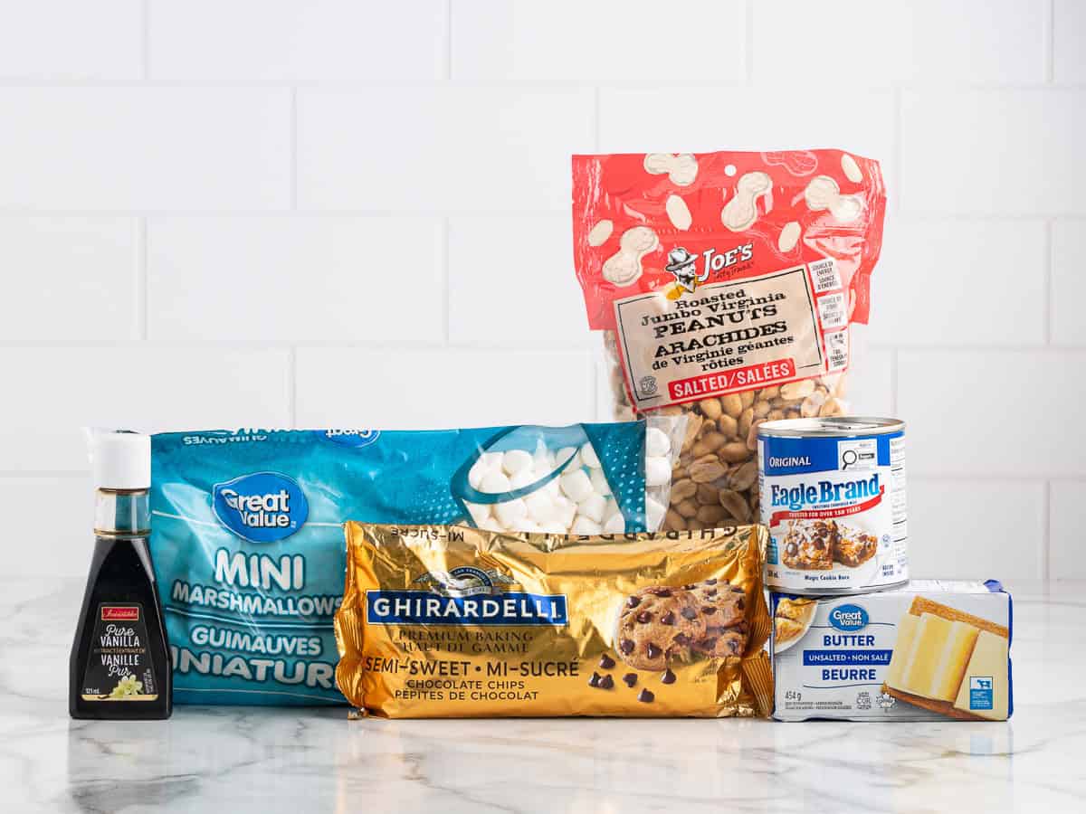 Assorted baking ingredients on a counter—vanilla extract, mini marshmallows, semi-sweet chocolate chips, salted peanuts, sweetened condensed milk, and a stick of butter, all in their packaging—perfectly set the stage for creating a classic Rocky Road Fudge Recipe.