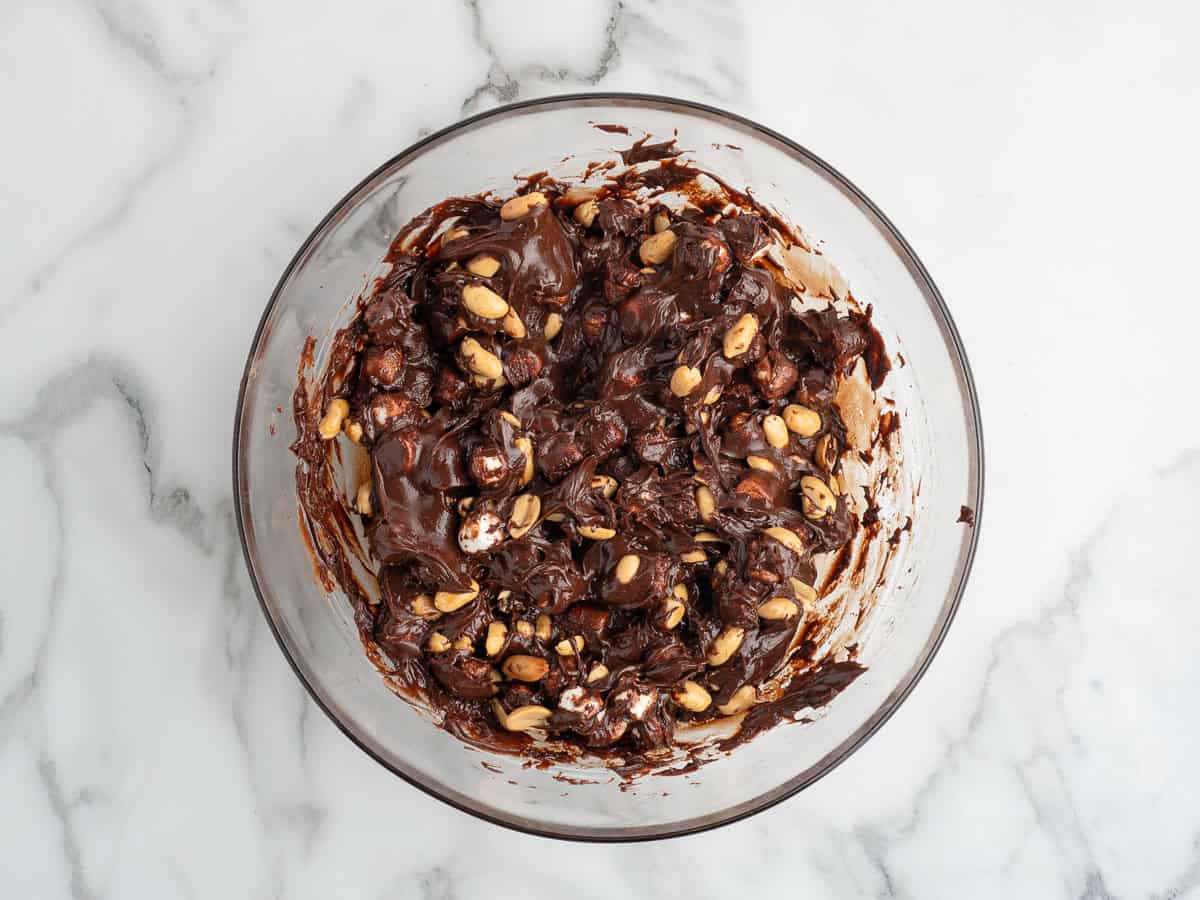 A glass bowl on a marble surface filled with a mixture of melted chocolate, mini marshmallows, and peanuts—the perfect start to a classic Rocky Road Fudge.