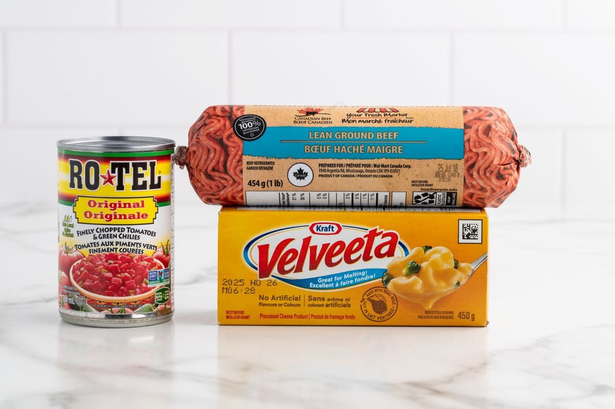 A can of Ro-Tel diced tomatoes and green chilies, lean ground beef, and Kraft Velveeta cheese are arranged on a white countertop—the classic ingredients for a flavorful Rotel Dip.