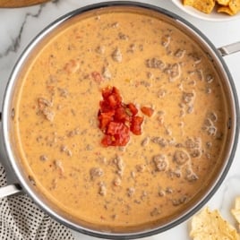 Overhead view of a saucepan filled with beefy Rotel dip, topped with diced tomatoes and served with chips.
