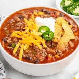 Overhead view of taco soup bowl with cheddar cheese, sour cream, jalapeño, and tortilla strips set against a background of the soup's surface.